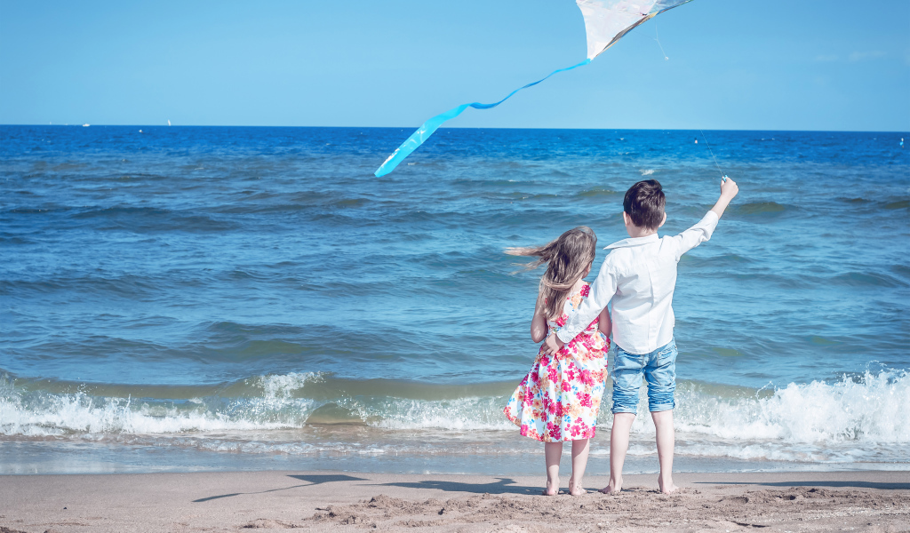 Маленькие мальчик и девочка запускаю воздушного змея на пляже
