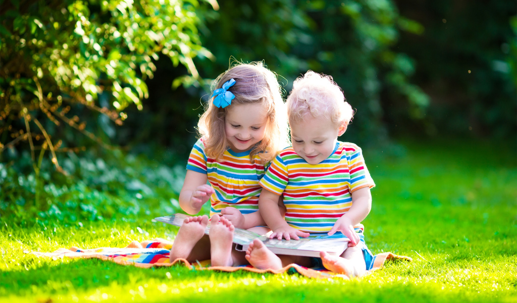 Маленькие мальчик и девочка читают книгу сидя на зеленой траве