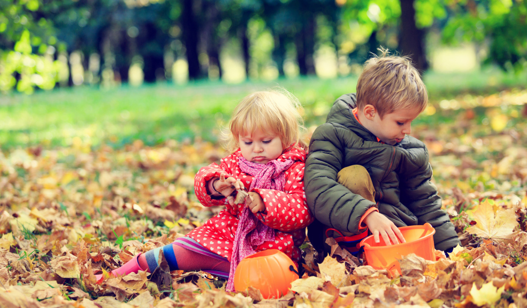Маленькие мальчик и девочка сидят на желтой листве в парке осенью