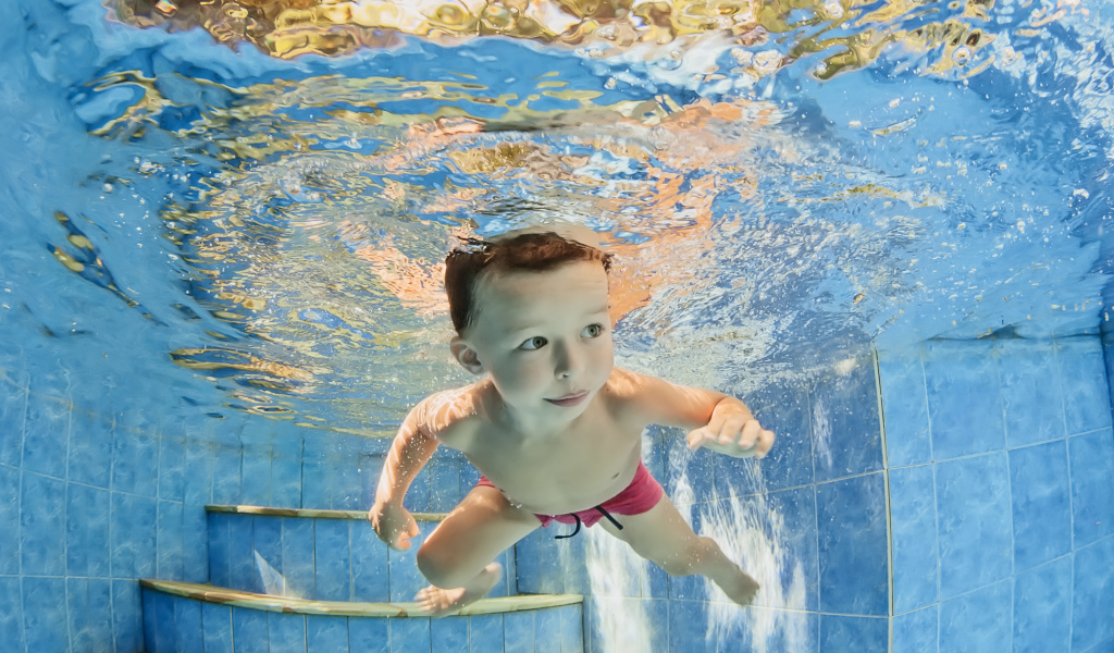Маленький мальчик плавает под водой в бассейне