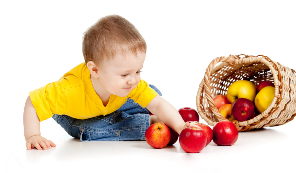 Маленький мальчик с корзиной спелых яблок на белом фоне