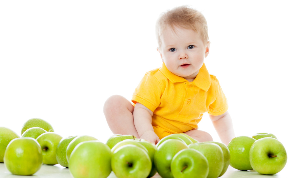 Маленький мальчик с зелеными яблоками на белом фоне