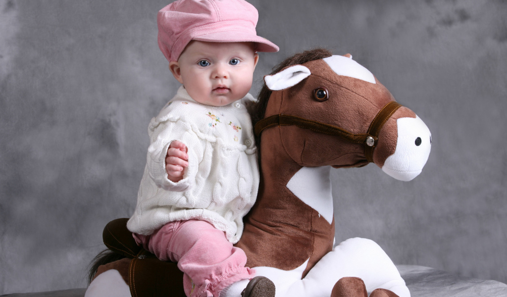 Маленький ребенок в розовой кепке сидит на игрушечной лошади
