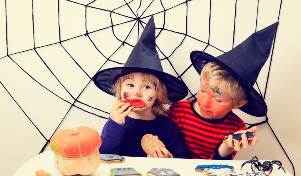 Маленькие дети в костюмах на Хэллоуин едят праздничные сладости