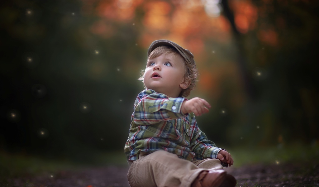 Маленький милый мальчик сидит в кепке на дороге