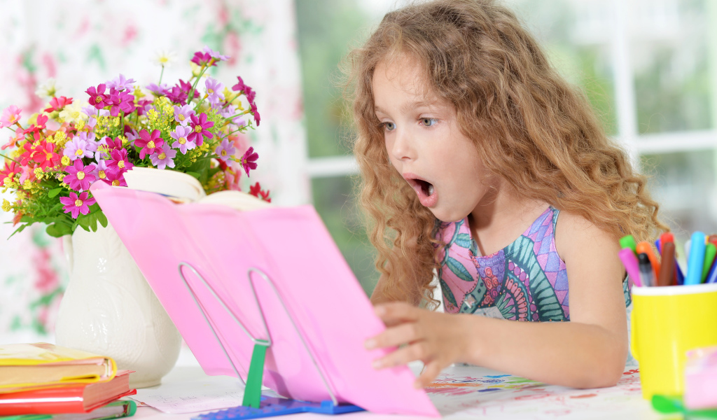 Маленькая русоволосая девочка удивленно смотрит в книгу