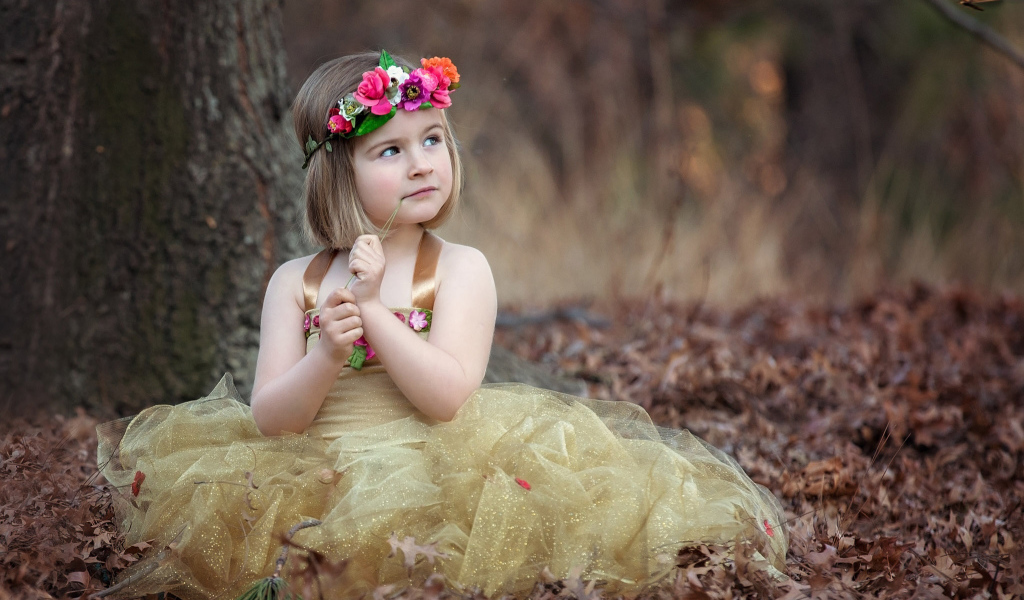 Маленькая девочка в красивом платье сидит на сухой листве