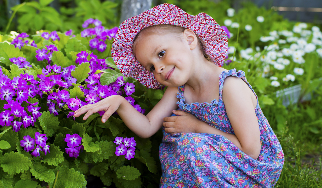 Маленькая девочка в шляпе рядом с фиолетовыми цветами