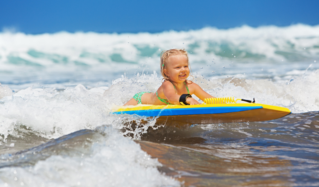 Маленькая девочка в море на доске для серфинга
