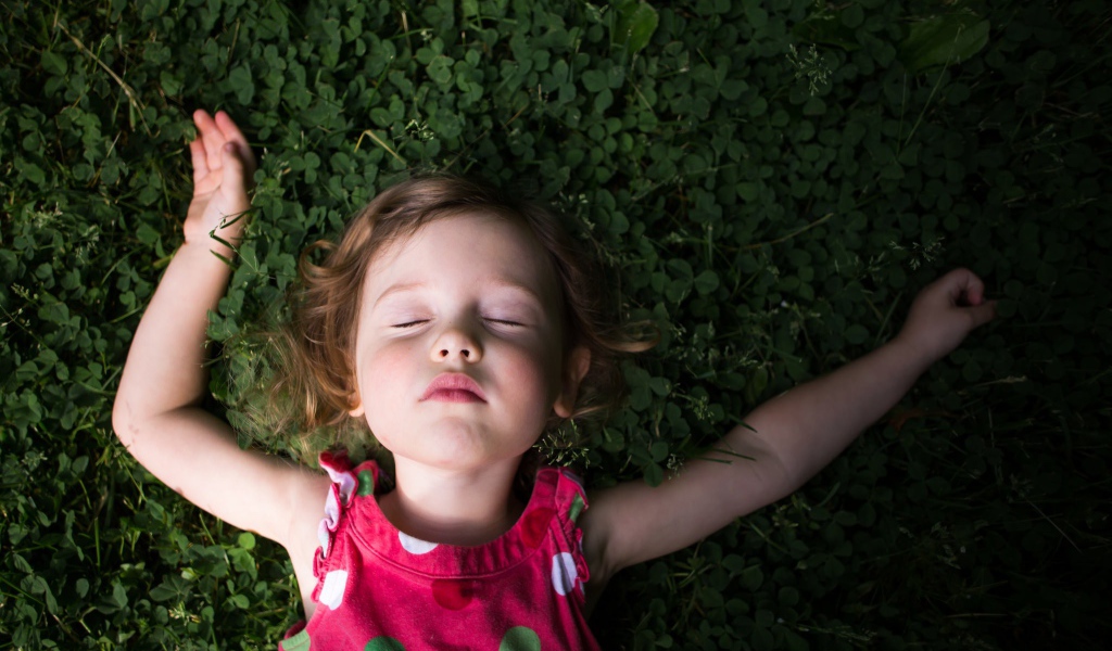 Маленькая девочка спит на зеленой траве 