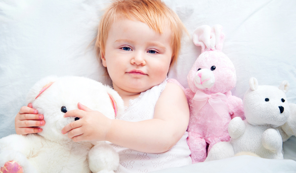 Маленькая девочка лежит в кровати с плюшевыми игрушками