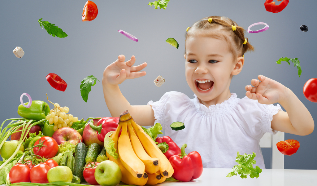 Маленькая девочка играет с овощами и фруктами на кухне