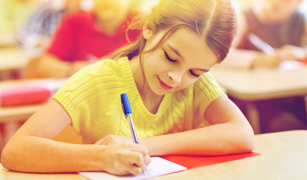 Маленькая девочка школьница пишет ручкой в тетради