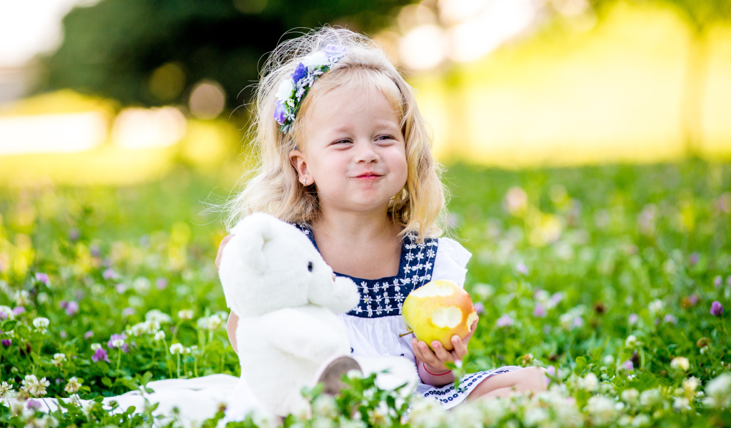 Маленькая девочка с белым медвежонком в руках и большим яблоком