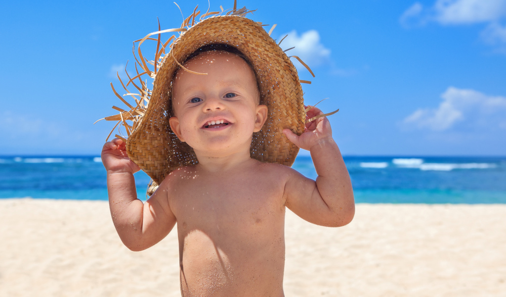 Маленький улыбающийся мальчик в соломенной шляпе на пляже