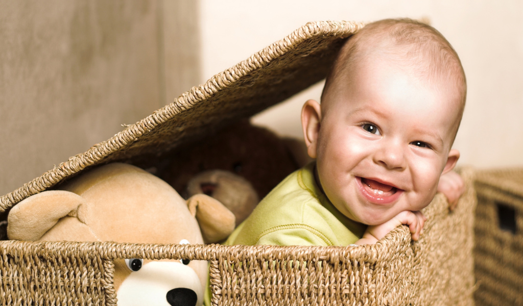 Маленький улыбающийся ребенок сидит в корзине с игрушками