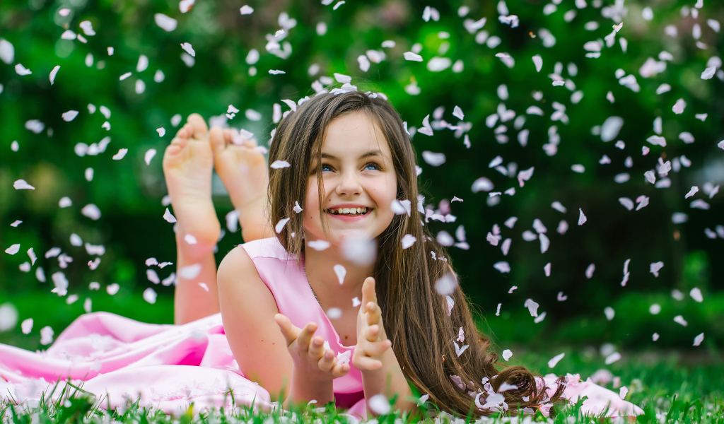 Маленькая улыбающаяся девочка шатенка ловит лепестки