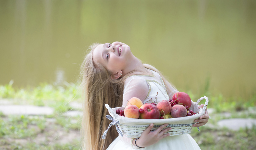 Маленькая улыбающаяся девочка в белом платье с корзиной фруктов