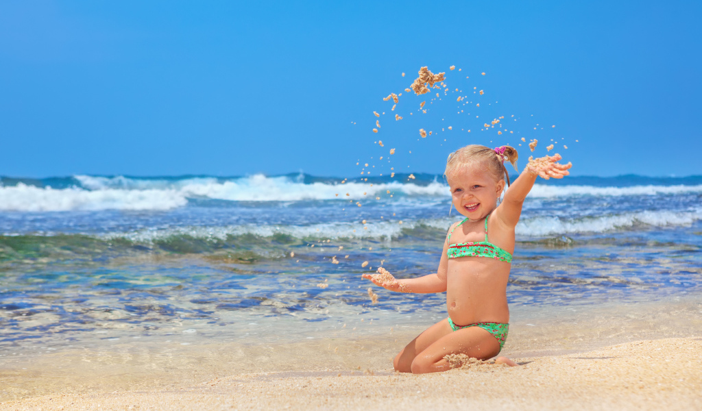 Маленькая улыбающаяся девочка играет на пляже с песком