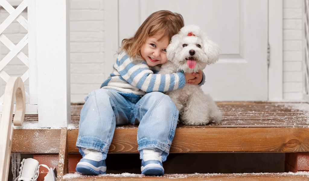Маленькая улыбающаяся девочка сидит с белым пуделем на ступеньках