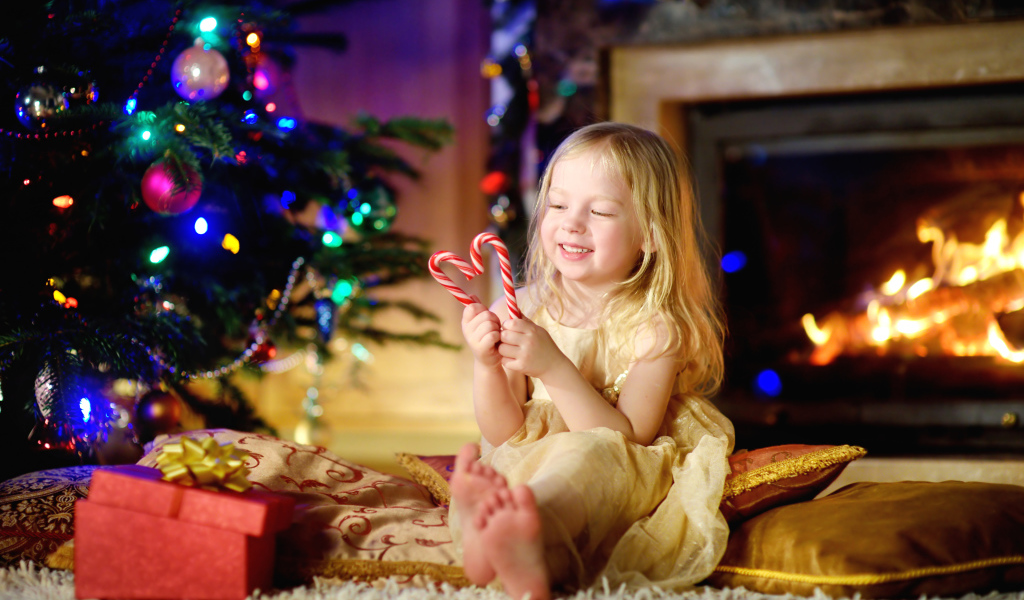 Длинноволосая девочка блондинка с леденцами у новогодней елки