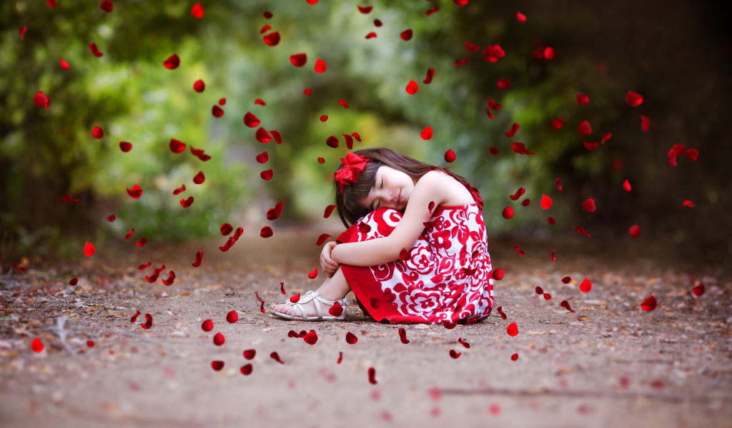 Лепестки красной розы падают на маленькую девочку