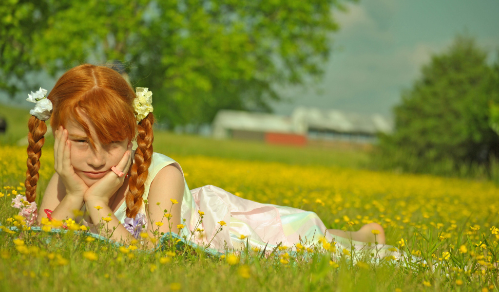 Рыжеволосая девочка с косичками лежит на зеленой траве