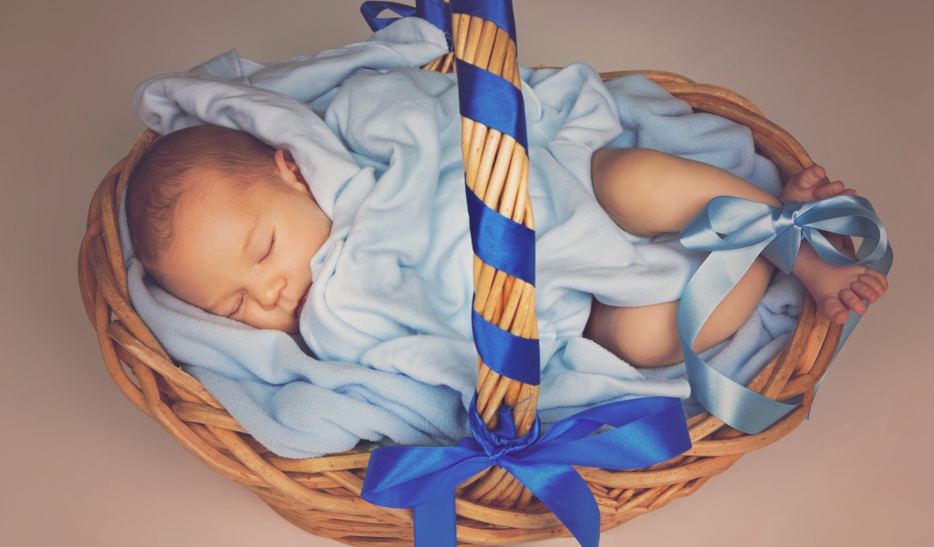 Спящий грудной ребенок в корзине с синими лентами