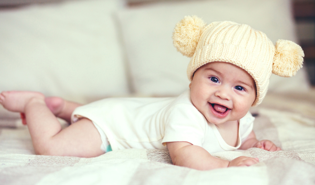 Улыбающийся грудной ребенок в забавной вязаной шапке