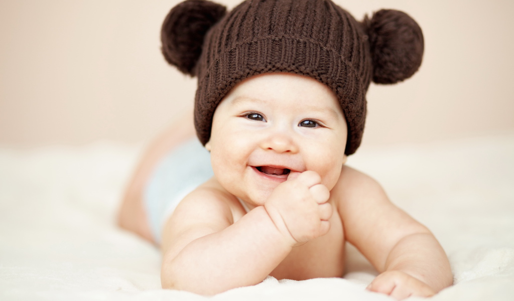 Улыбающийся грудной ребенок в коричневой вязаной шапке