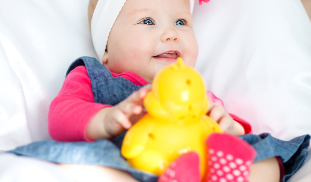 Улыбающаяся голубоглазая девочка младенец с игрушкой в руках