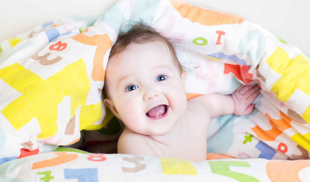 Улыбающийся голубоглазый ребенок под разноцветным покрывалом