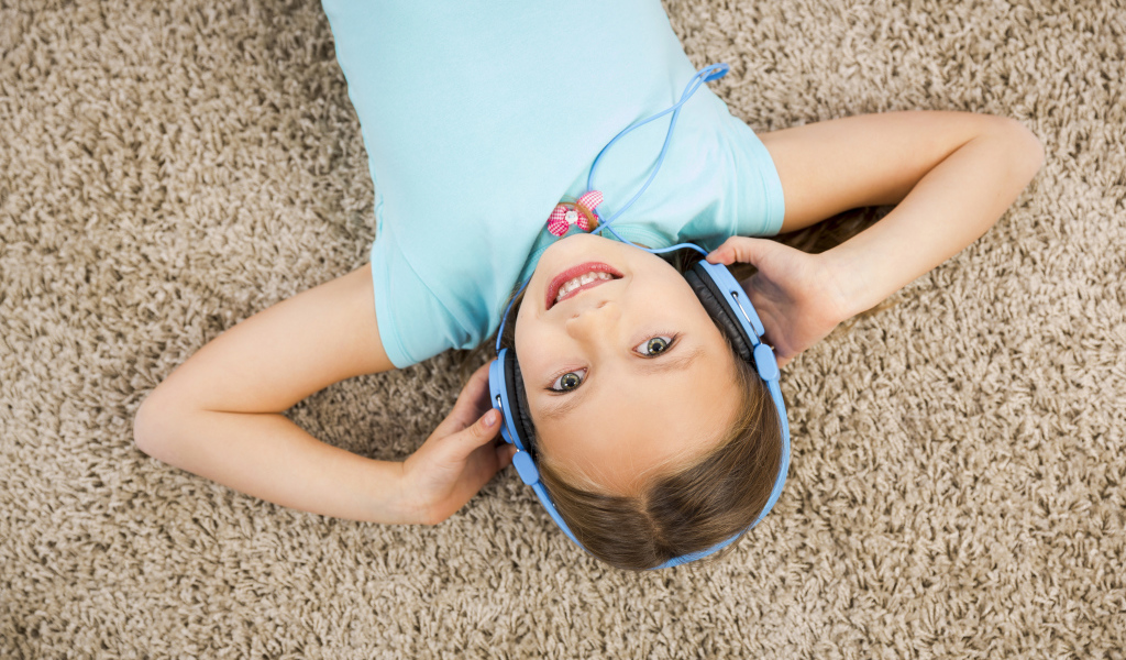 Улыбающаяся девочка в больших голубых наушниках