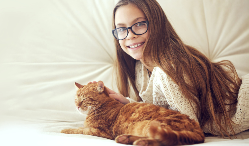 Улыбающаяся девочка шатенка в очках гладит рыжего кота