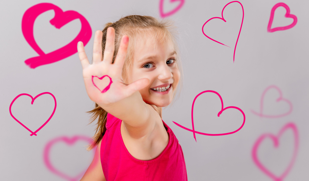 Улыбающаяся девочка с нарисованными сердечками на сером фоне