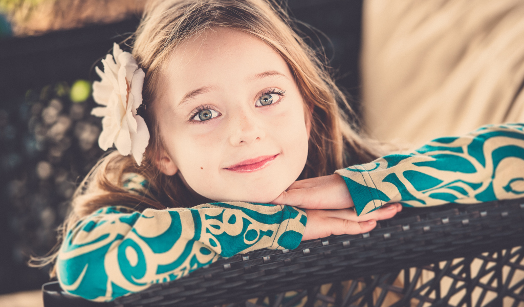 Улыбающаяся зеленоглазая девочка с белым цветком в волосах