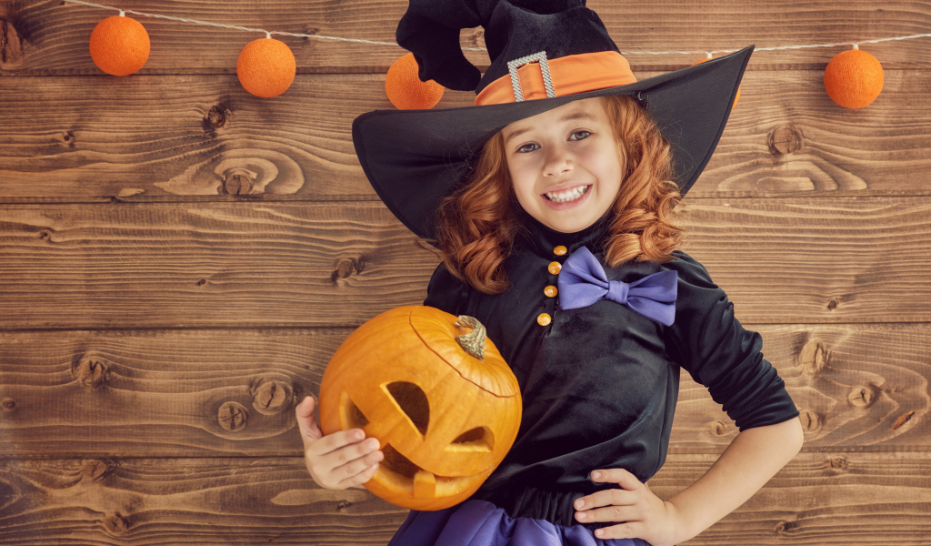 Улыбающаяся маленькая девочка в костюме ведьмы с тыквой на Хэллоуин