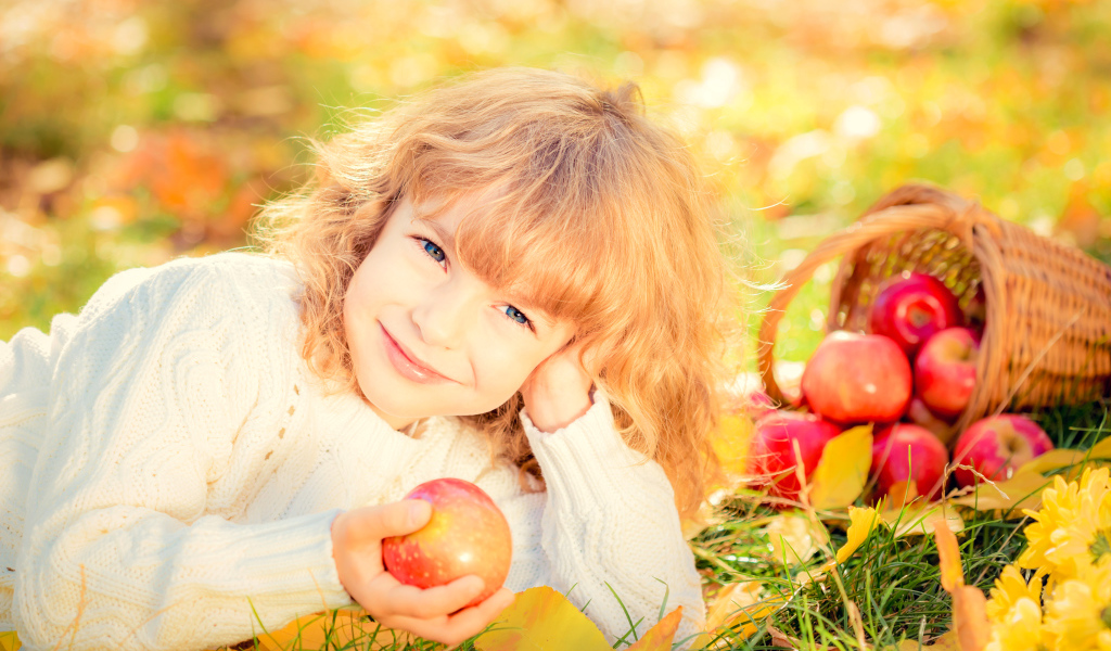 Улыбающаяся рыжеволосая девочка с корзиной красных яблок