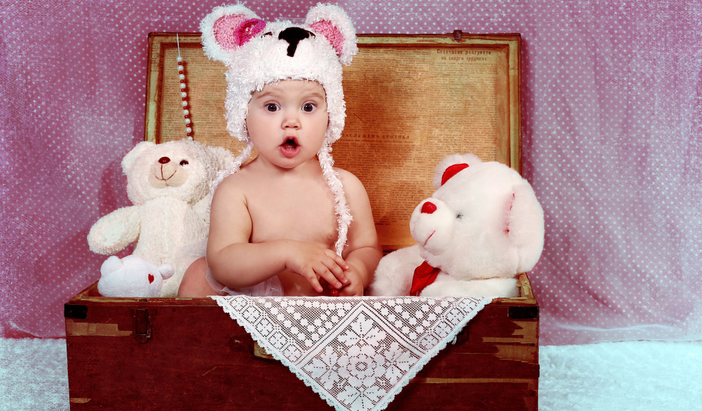 Удивленный малыш сидит в сундуке с мягкими игрушками