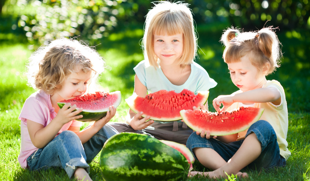 Три маленькие девочки едят арбуз на зеленой траве летом
