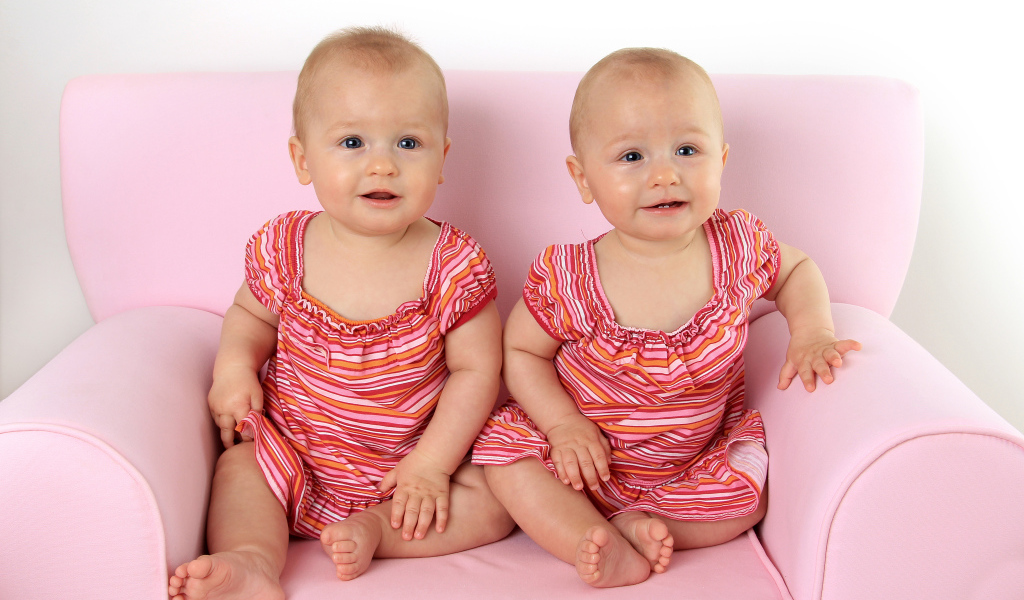 Две милые маленькие девочки сидят на розовом диване