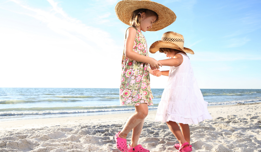 Две маленькие девочки танцуют на песке на пляже