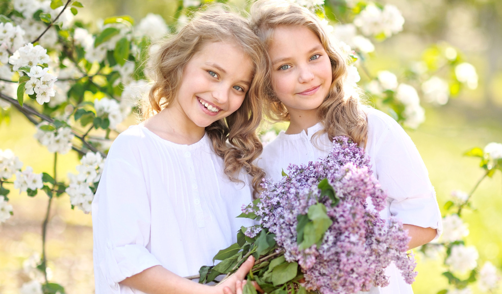 Две улыбающиеся девочки близняшки с букетом сирени