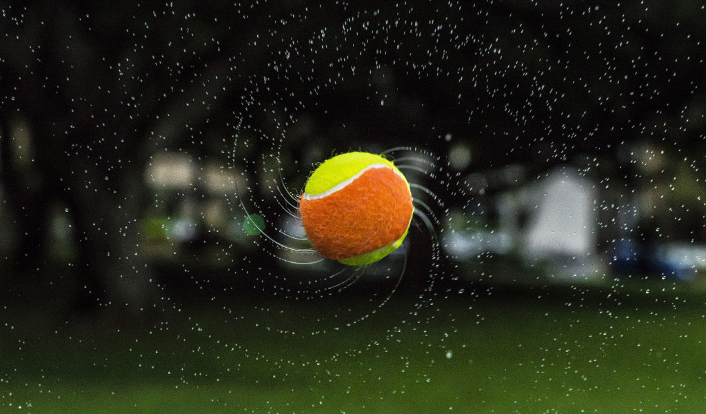 Теннисный мяч летит в каплях воды 