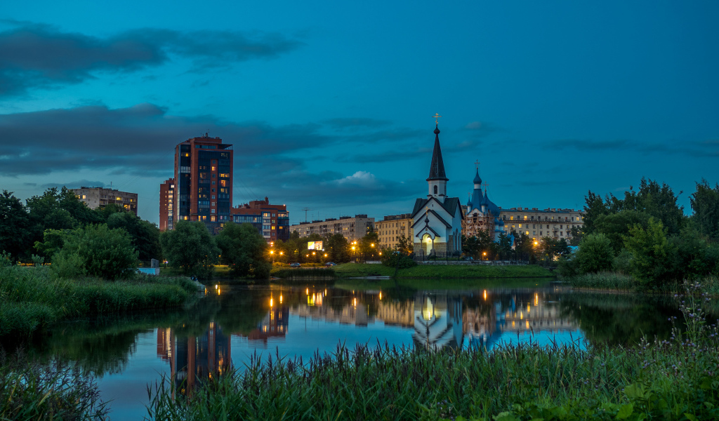 Вечерние огни маленькой церкви и домов отражаются в воде городского пруда, Санкт-Петербург. Россия