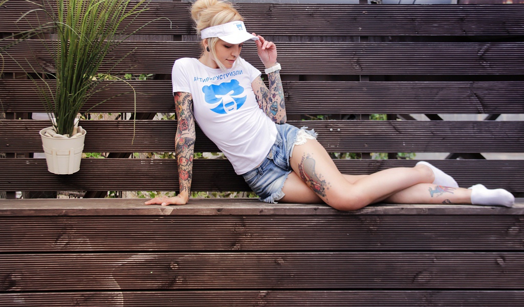 Спортивная девушка в татуировках лежит на деревянной лавке