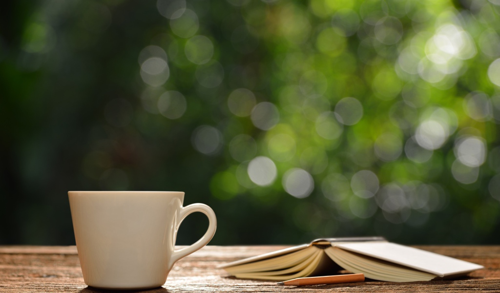 Белая чашка на столе с открытой книгой