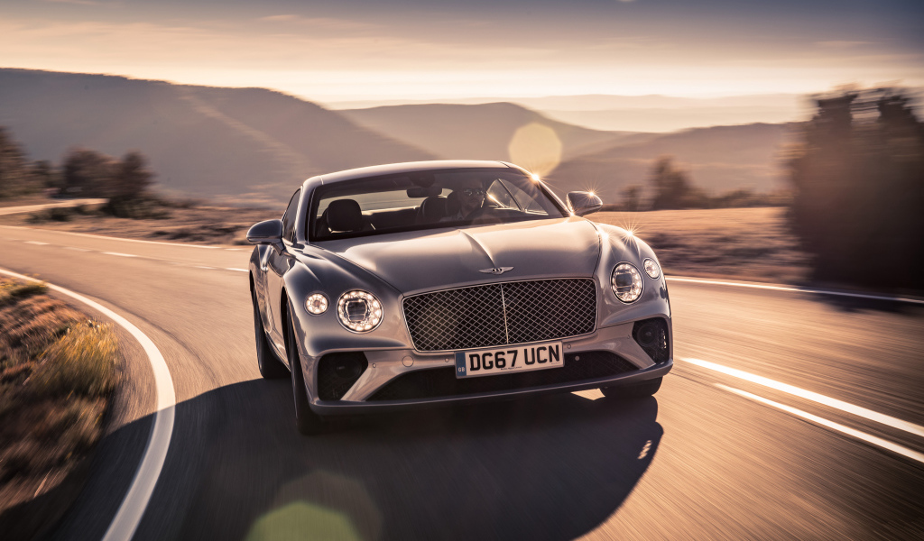 Серебристый автомобиль Bentley Continental GT 2018 года на трассе