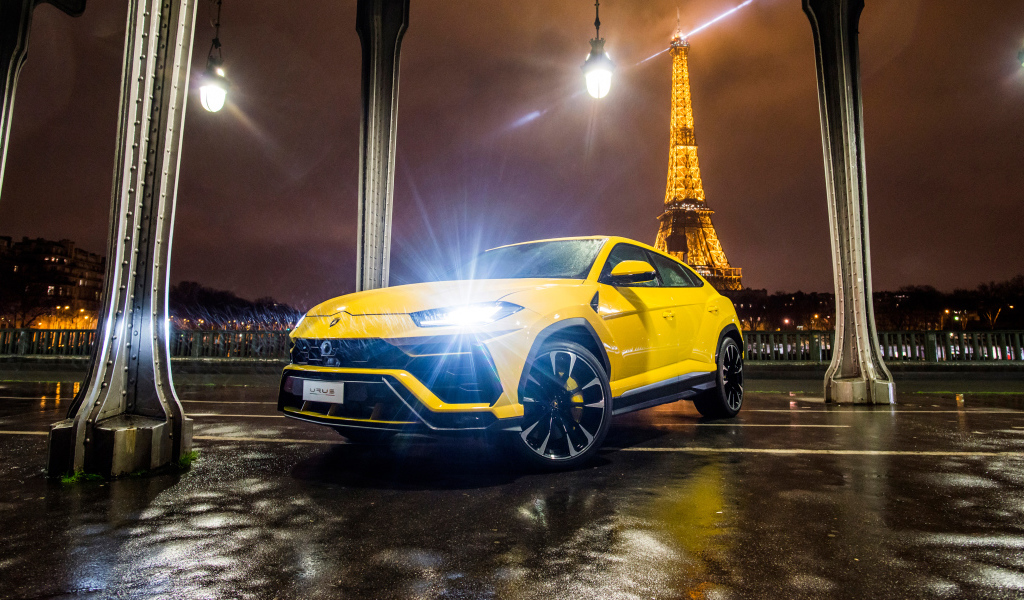 Желтый Lamborghini Urus, 2018 с включенными фарами на фоне Эйфелевой башни