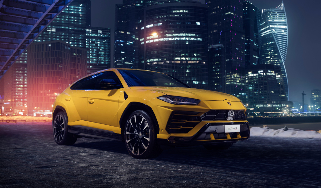 Желтый Lamborghini Urus на фоне ночных небоскребов